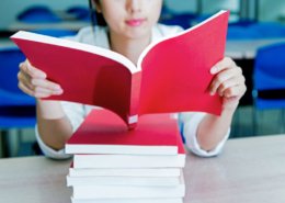 young woman reading a red book on a stack of other red books